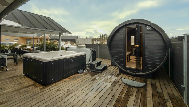 A hot tub and sauna on a wooden deck with a covered seating area and a view of the surrounding landscape. - Nice home in Grenaa with sauna (Grenaa)
