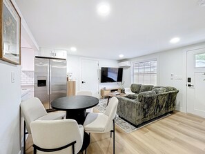 A modern living room with a dining area, a sofa, a flat-screen TV, and a kitchen with a refrigerator. - Sunny Nokomis Getaway•Private Pool•Backyard Oasis (Nokomis)