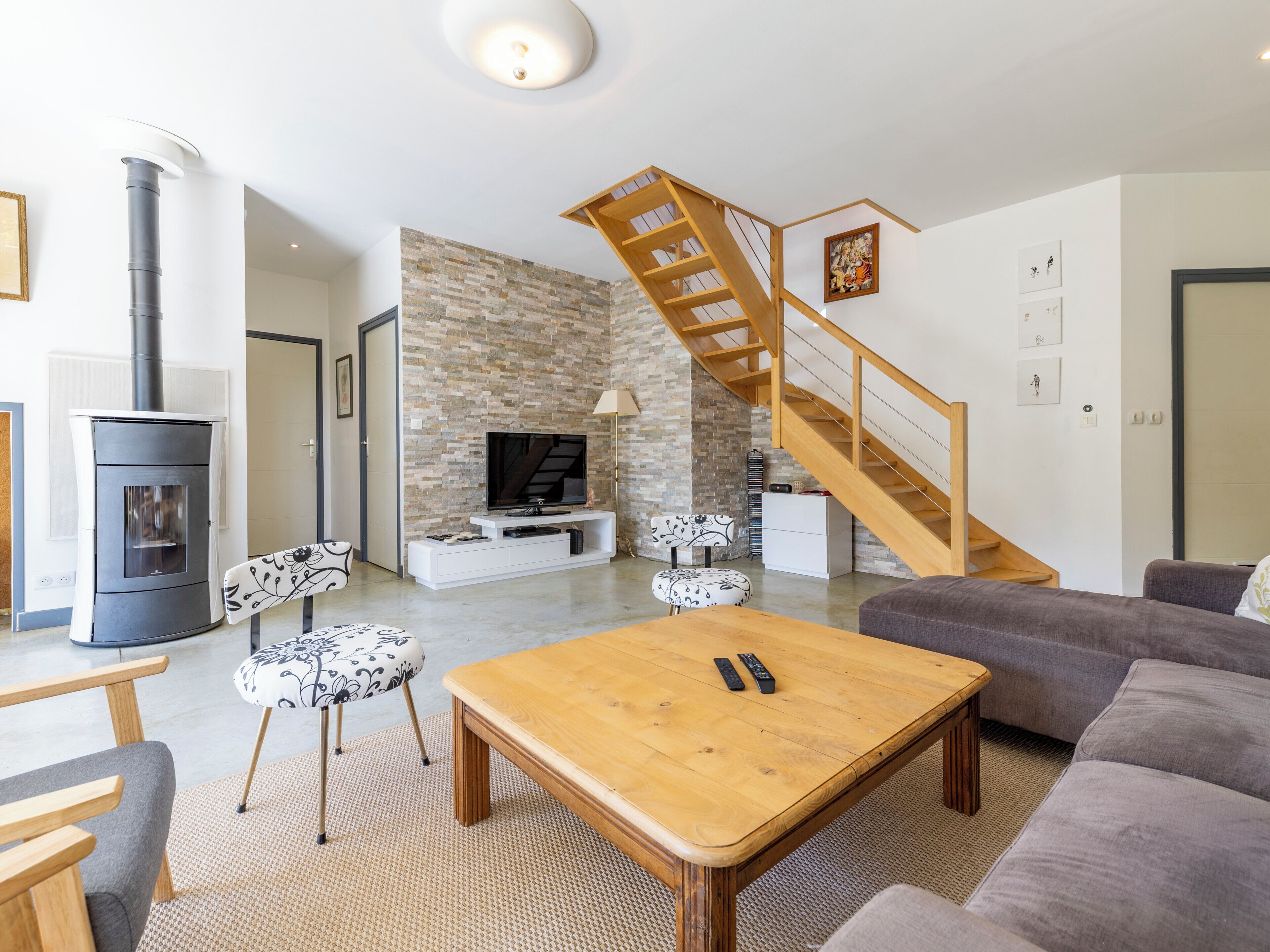 A modern living room with a fireplace, a TV, a wooden staircase, and a sofa.