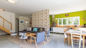 Un salon moderne comprenant un canapé, des fauteuils, une table basse et un coin cuisine avec une table à manger et des chaises.