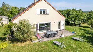 Une maison à deux étages avec un patio, un coin repas et un jardin.