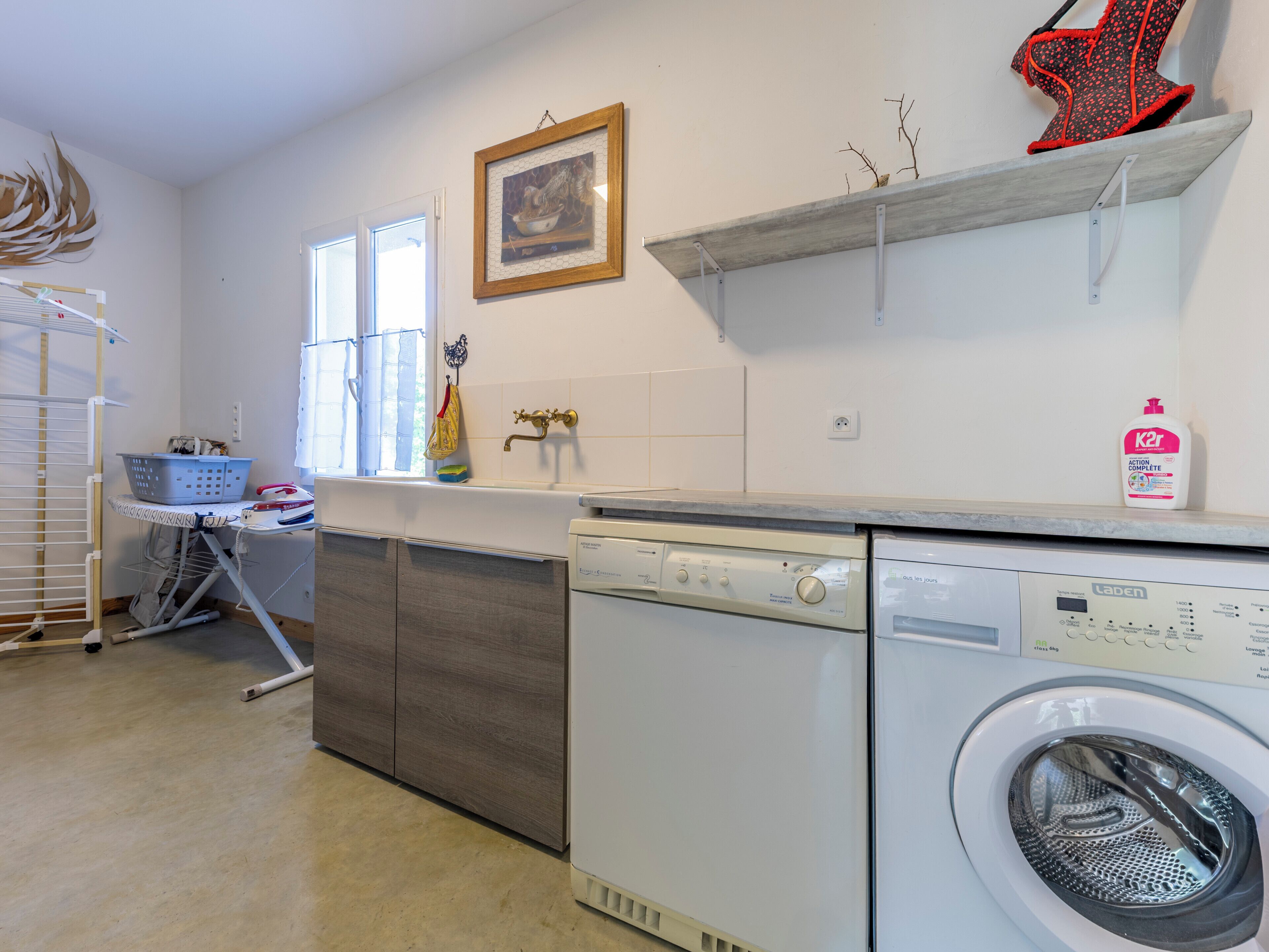 A laundry area with a washing machine, a drying rack, and a window with curtains.