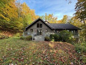 A modern house with a large deck, surrounded by autumn foliage.