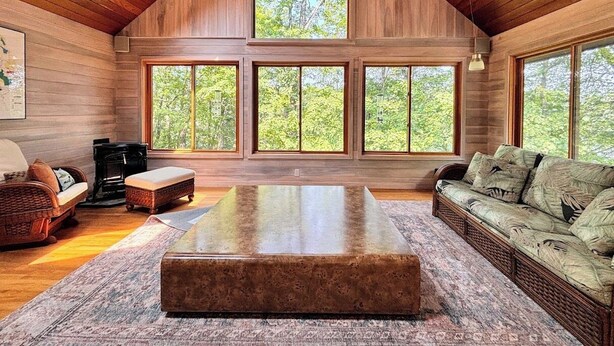 A spacious room with a high ceiling, large windows, a wooden floor, a central coffee table, a sofa, and a fireplace. - Lakefront Cabin Escape  Pristine Waters & Fall Foliage (Norfolk)