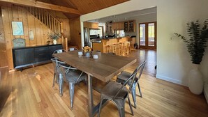 A spacious kitchen with wooden cabinets, a large island with stools, and a dining area with metal chairs. - Lakefront Cabin Escape  Pristine Waters & Fall Foliage (Norfolk)