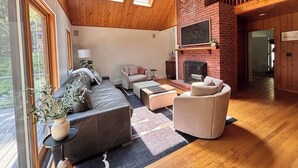A spacious living room with a fireplace, wooden ceiling, and large windows. - Lakefront Cabin Escape  Pristine Waters & Fall Foliage (Norfolk)