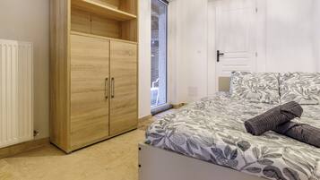 A bedroom with a bed, a wooden wardrobe, a radiator, and a window.