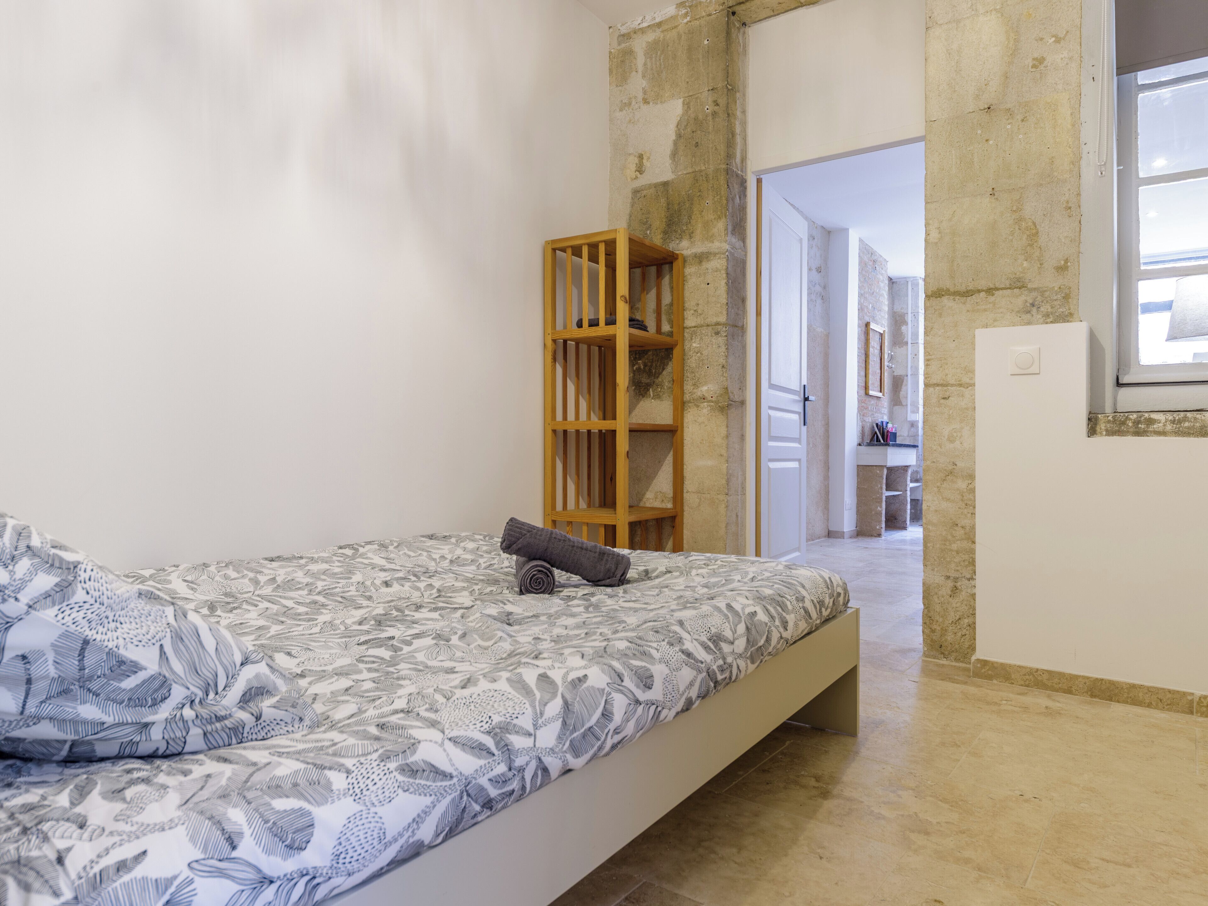 Ein Schlafzimmer mit einem Bett, einer Holzregaleinheit und einem durchgegangenen Tür erkennbaren Badezimmer.