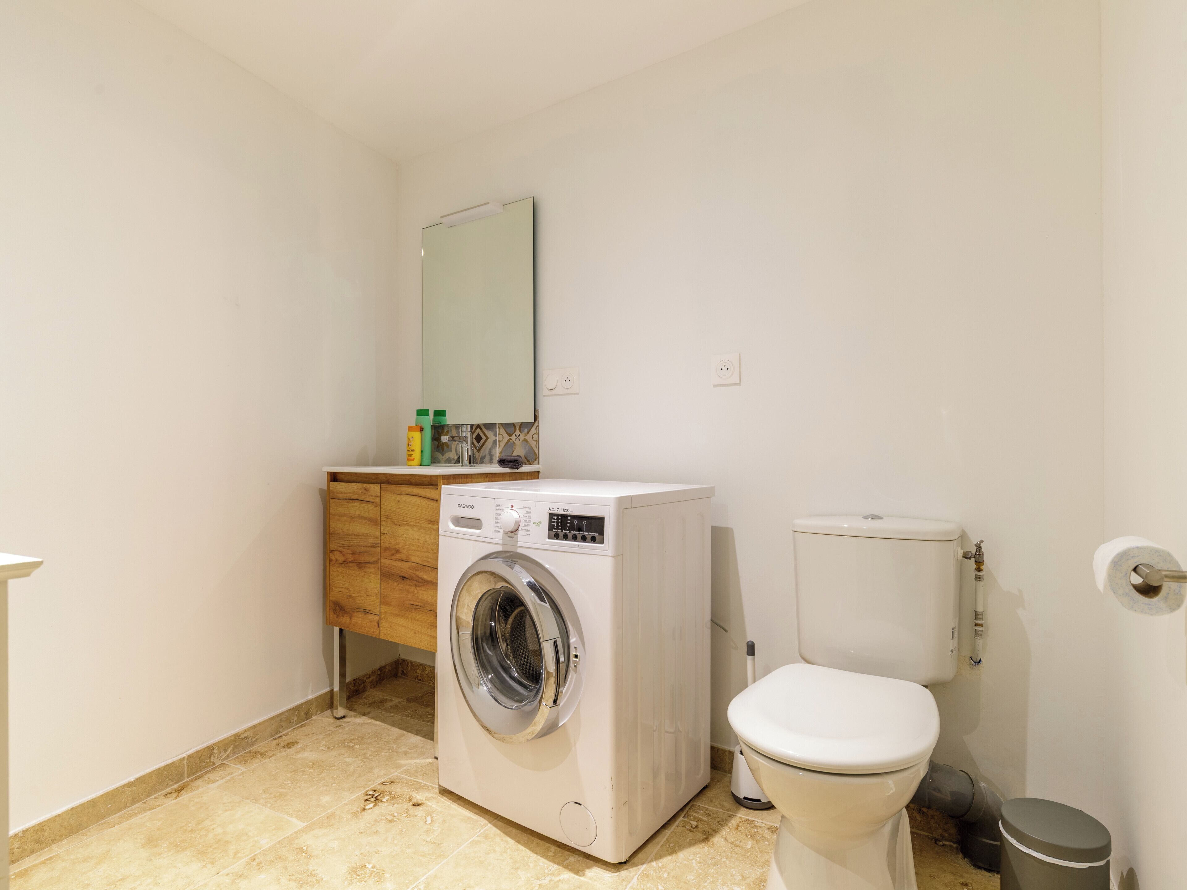 A compact bathroom with a washing machine, toilet, and a small cabinet with toiletries.