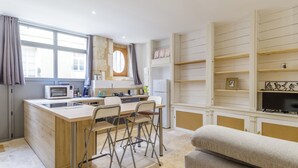 A compact kitchen with a microwave, sink, and bar area. There are foldable chairs and a sofa in the living area.