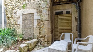 A stone-walled courtyard with a wooden door, a white wicker table, and two white plastic chairs.