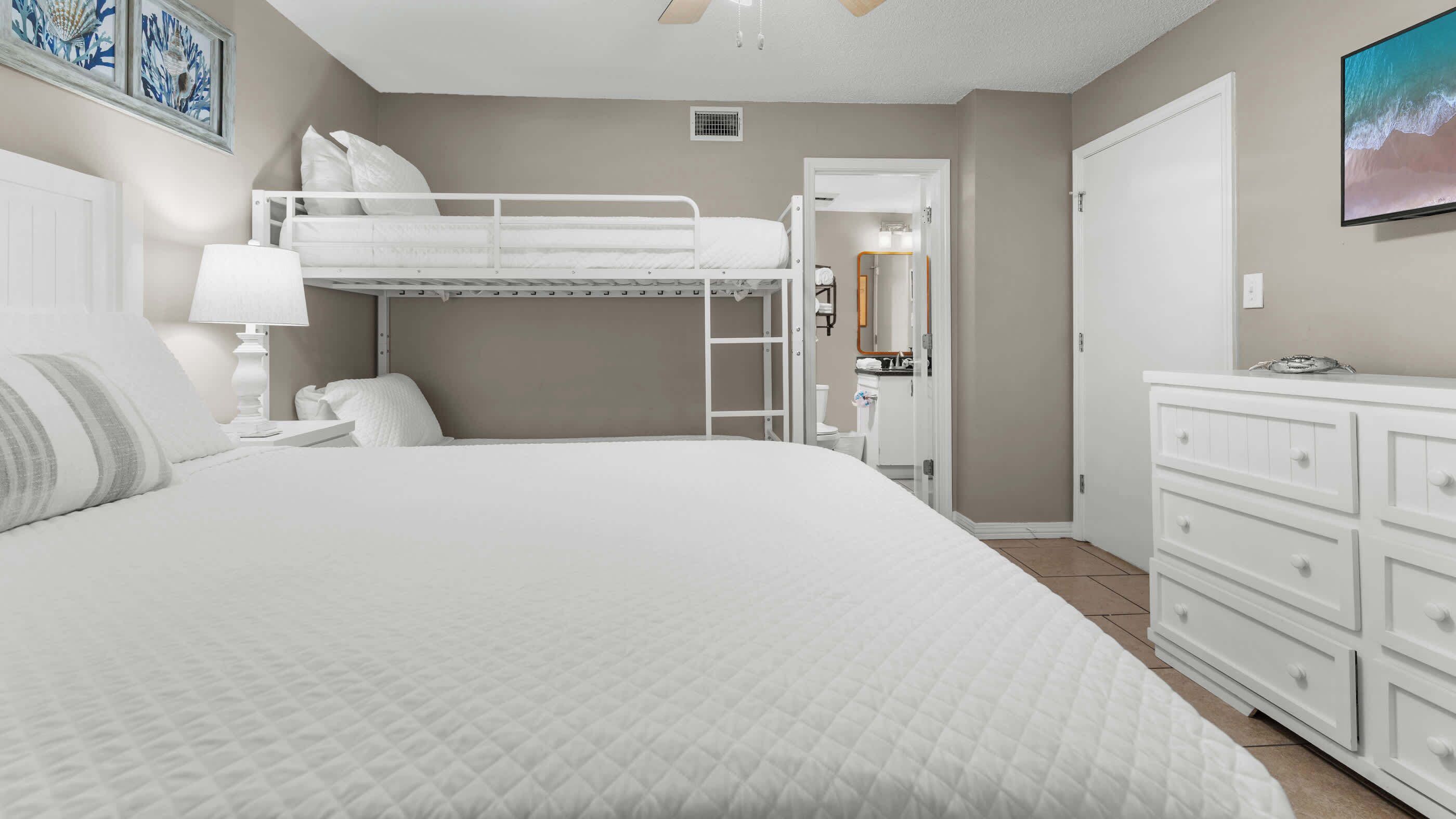 A bedroom with a bunk bed, a white dresser, and a painting on the wall.