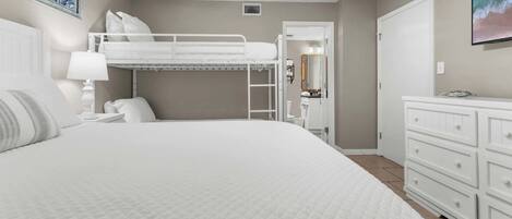 A bedroom with a bunk bed, a white dresser, and a painting on the wall.