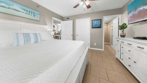 Ein Schlafzimmer mit einem Bett, einem Deckenventilator, einem Badezimmer mit Dusche und einem an der Wand montierten Fernseher.