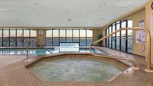 Ein beheiztes Hallenbad mit Whirlpool, umgeben von großen Fenstern mit Blick auf die Stadtlandschaft.