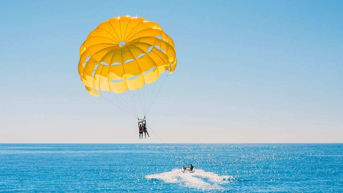 A person parasailing over a body of water with a yellow parachute.
