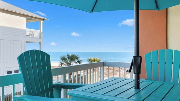 Ein Balkon mit türkisfarbenen Stühlen und einem Tisch mit Blick auf Strand und Meer.