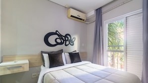 Un dormitorio con cama, mesita de noche, aire acondicionado y ventana con cortinas.