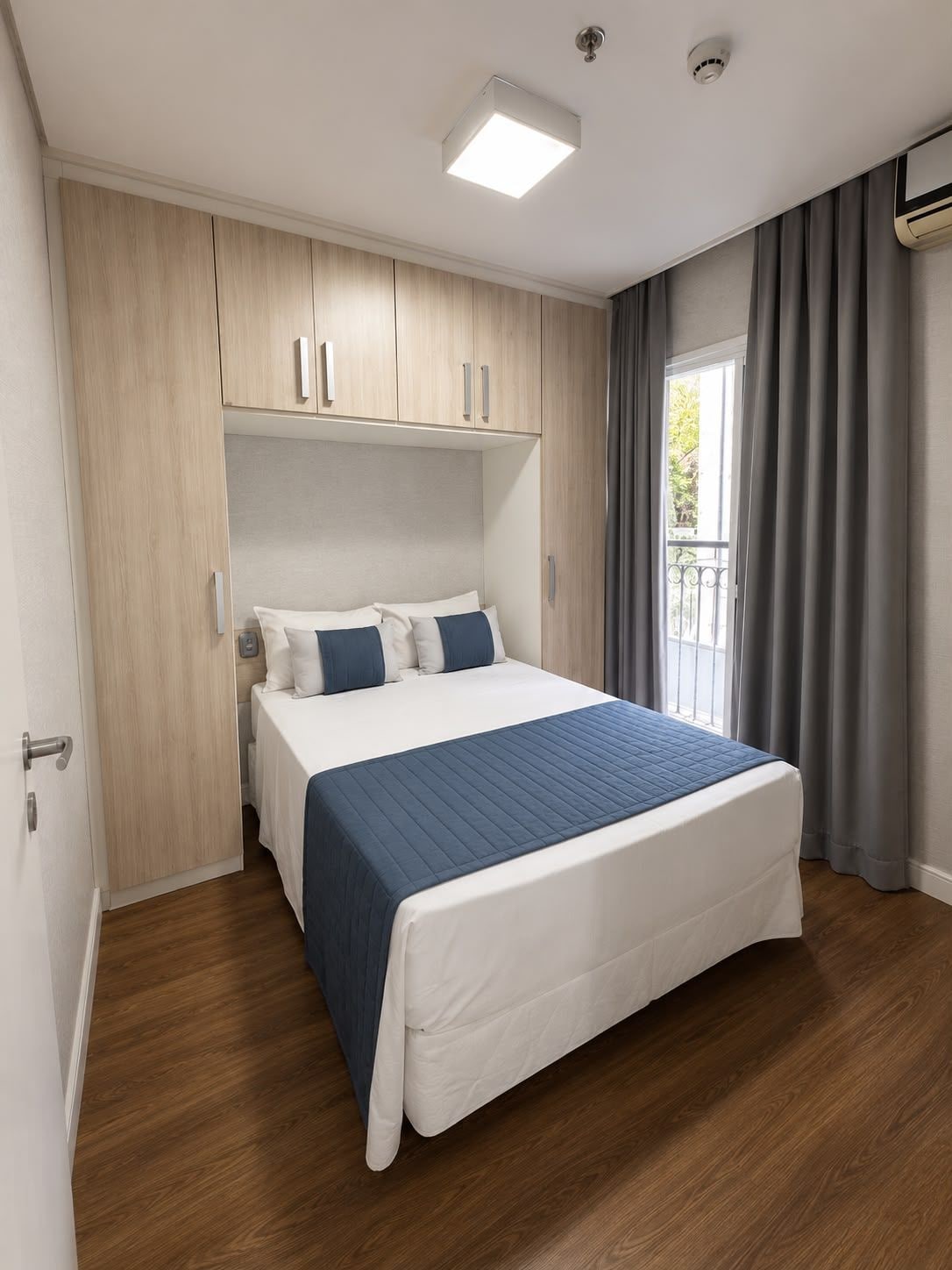 A bedroom with a bed, wooden wardrobe, and a window with curtains.
