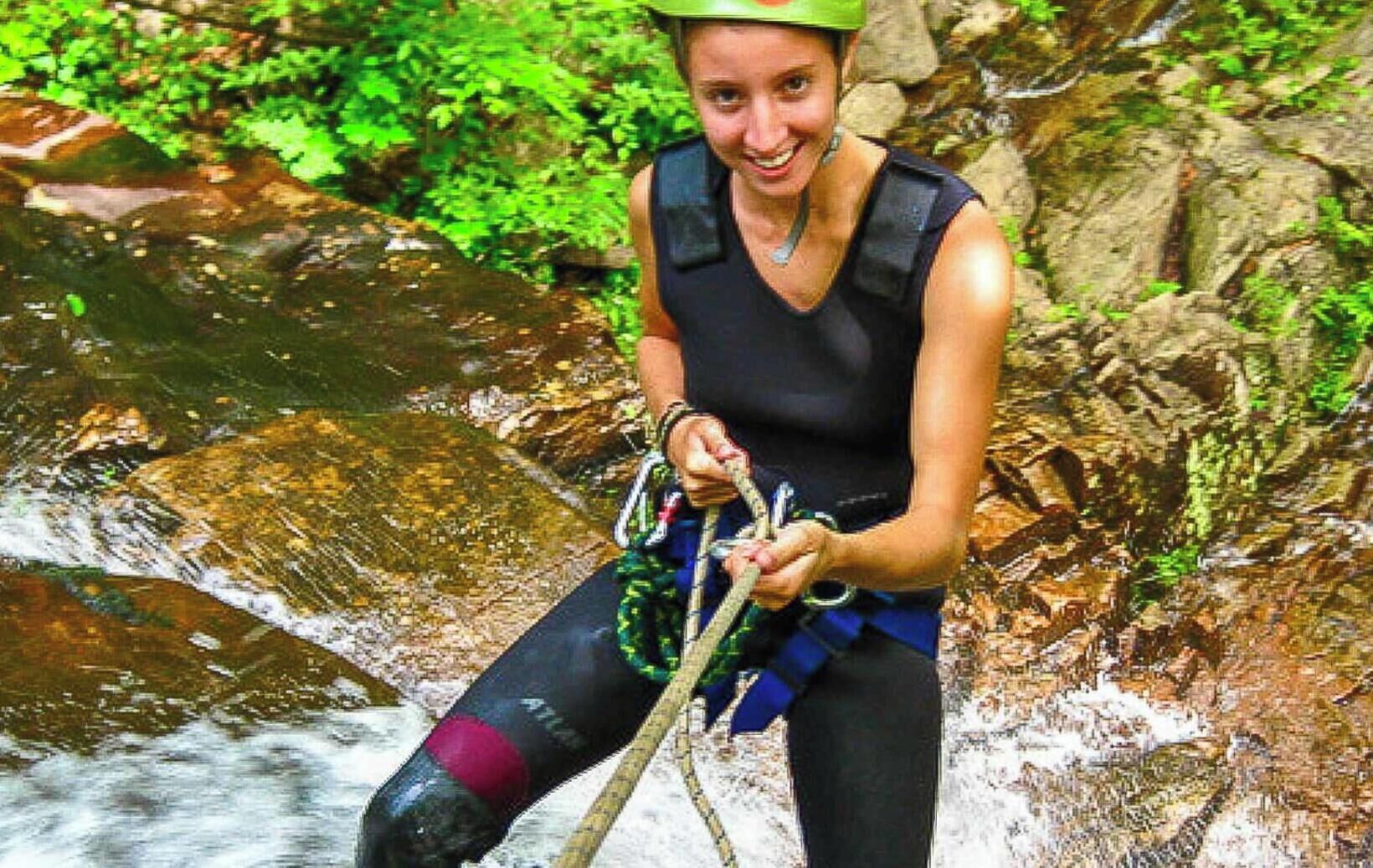 Una persona descendiendo por un arroyo rocoso usando arnés y cuerdas.