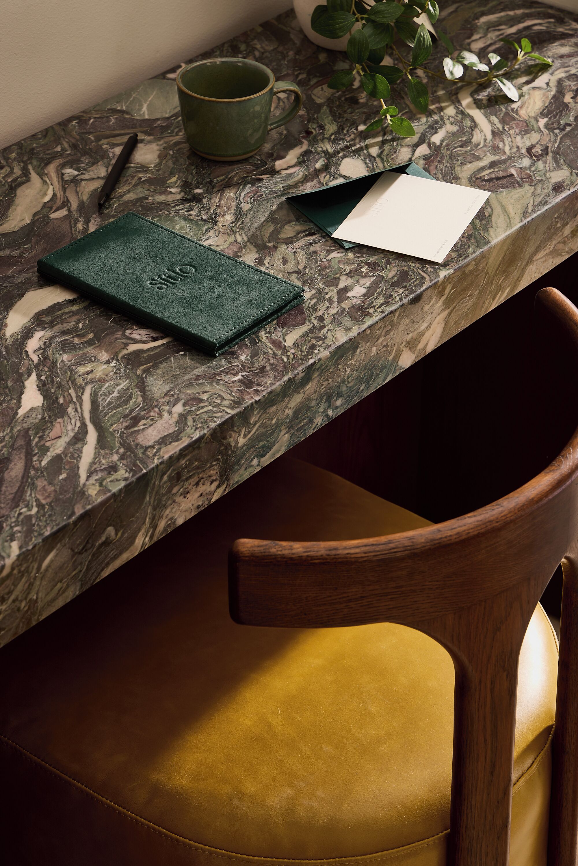 A marble countertop with a notebook, pen, mug, and plant.
