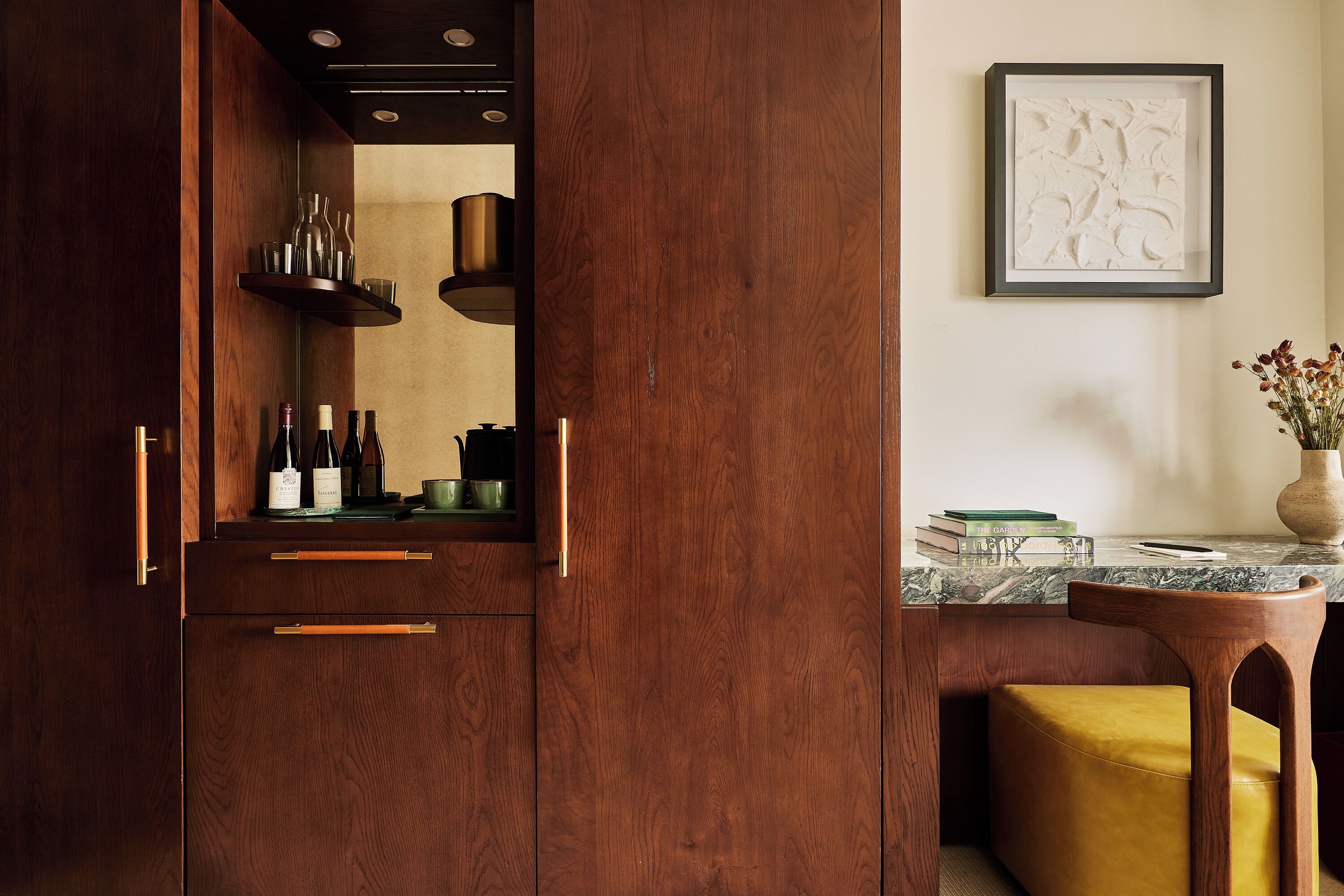 A wooden kitchen with a built-in oven, a marble countertop, and a framed artwork on the wall.