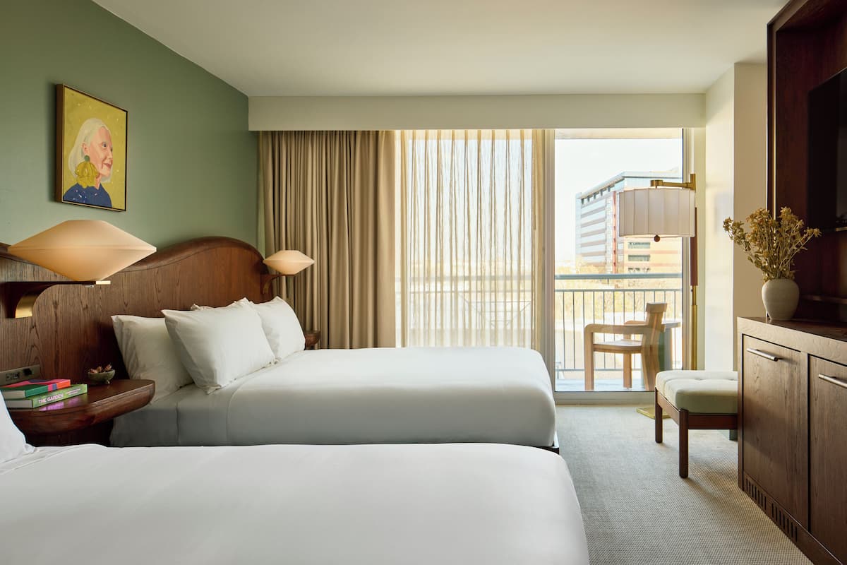 Une chambre d’hôtel avec deux lits, un bureau, une chaise, une télévision et une fenêtre donnant sur un immeuble.