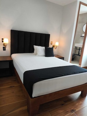 Una habitación de hotel con una cama grande, dos mesitas de noche y un espejo.