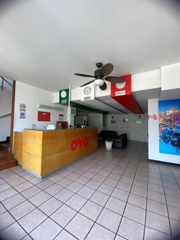 A reception area with a wooden counter labeled "OYO," a ceiling fan, and a clock. - Hotel Sicilia (Aguascalientes)