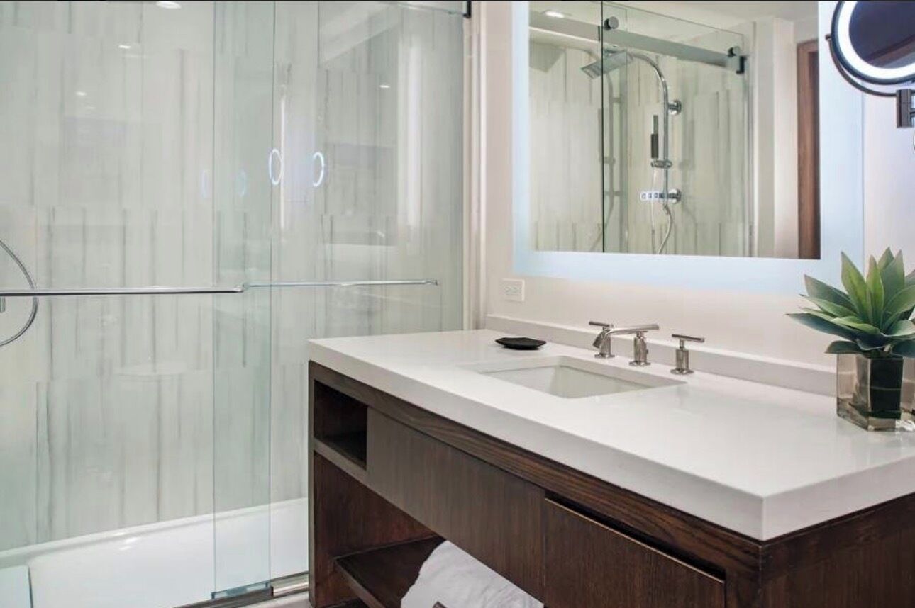 A modern bathroom with a glass shower enclosure, a white sink vanity, and a mirror with a ring light.