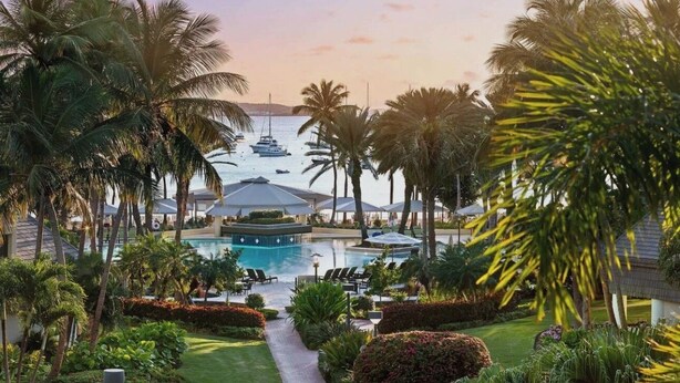 Ein Resort mit einem zentral gelegenen Pool, umgeben von Palmen und Liegestühlen.