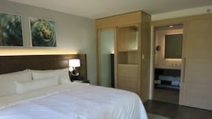 Ein Hotelzimmer mit einem großen Bett, einem Nachttisch, einer Lampe, einem Kleiderschrank und einem durchgegangenen Tür erkennbaren Badezimmer.