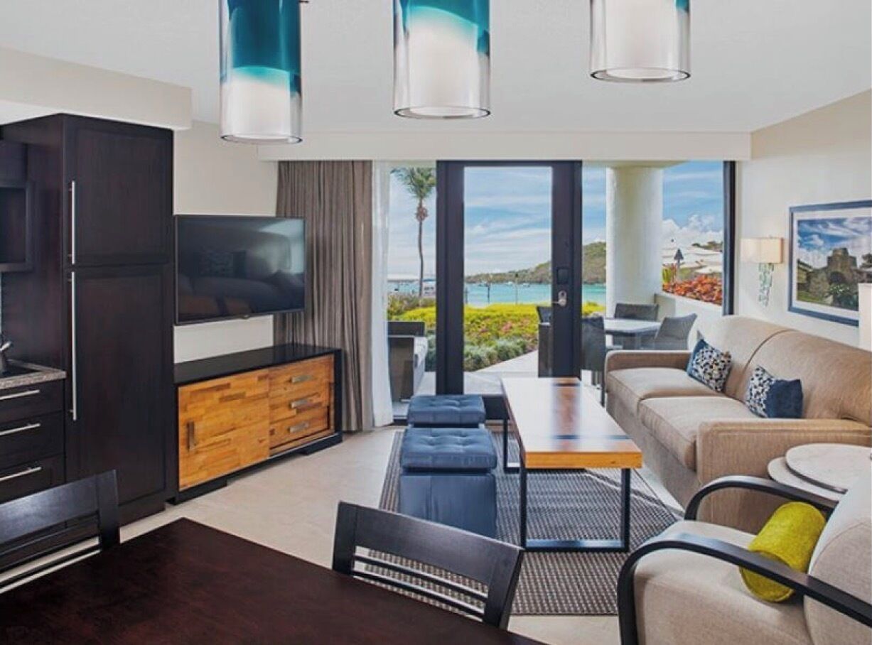 Una sala de estar moderna con televisor de pantalla plana, mueble de madera, sofá oscuro y vista al mar.