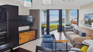 Ein modernes Wohnzimmer mit Flachbildfernseher, Holzschrank, dunklem Sofa und Meerblick.