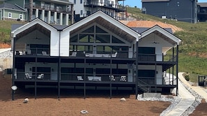 Ein modernes, zweistöckiges Haus mit Balkon, einer Holzterrasse und einem Kiesweg, der zu einem Steg führt.