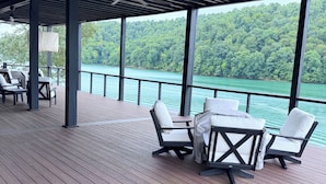 Eine überdachte Terrasse mit Gartenmöbeln, einem Deckenventilator und Blick auf einen bewaldeten See.