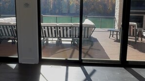 Blick durch große Glastüren auf eine Terrassenanlage mit Pool, Sitzgelegenheiten und einer Steinmauer.