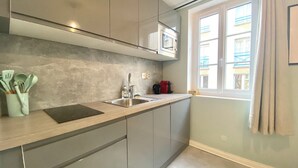 A modern kitchen with grey cabinets, a stainless steel sink, and a window with curtains. - Le 202 : studio rénové au coeur de Rouen (Rouen)