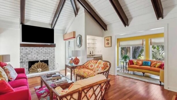 Un salon spacieux avec une cheminée, un canapé rouge, un fauteuil en osier et un divan jaune.