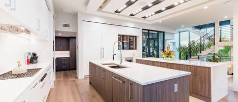 A modern kitchen with white cabinetry, a central island, and a built-in stove.