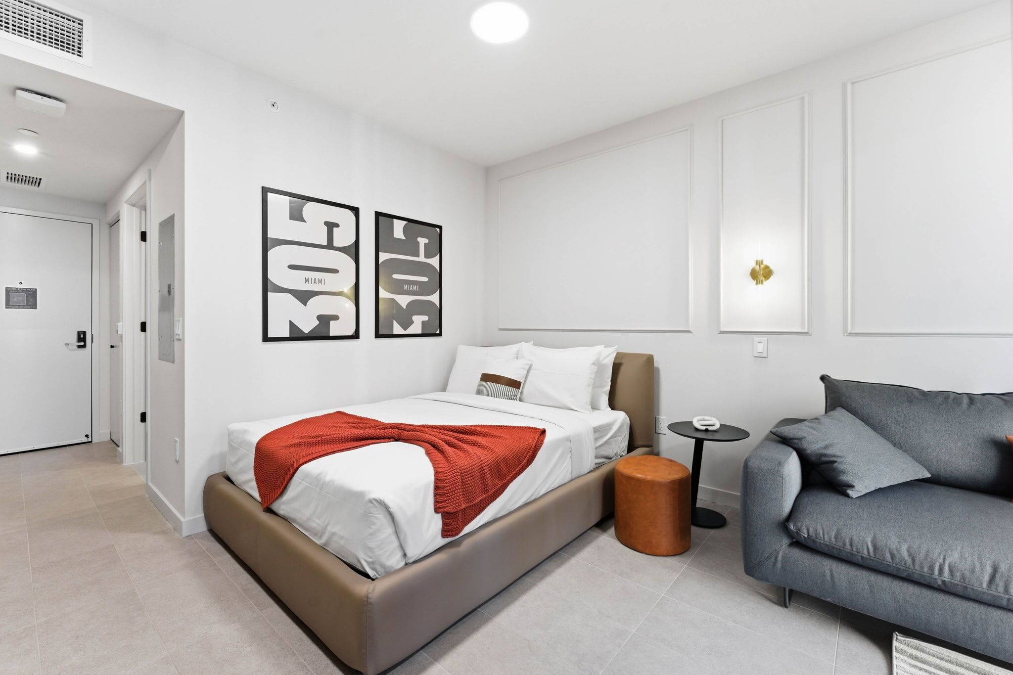 Una habitación de hotel moderna con una cama, un sofá gris y una mesita redonda.