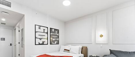 Una habitación de hotel moderna con una cama, un sofá gris y una mesita redonda.