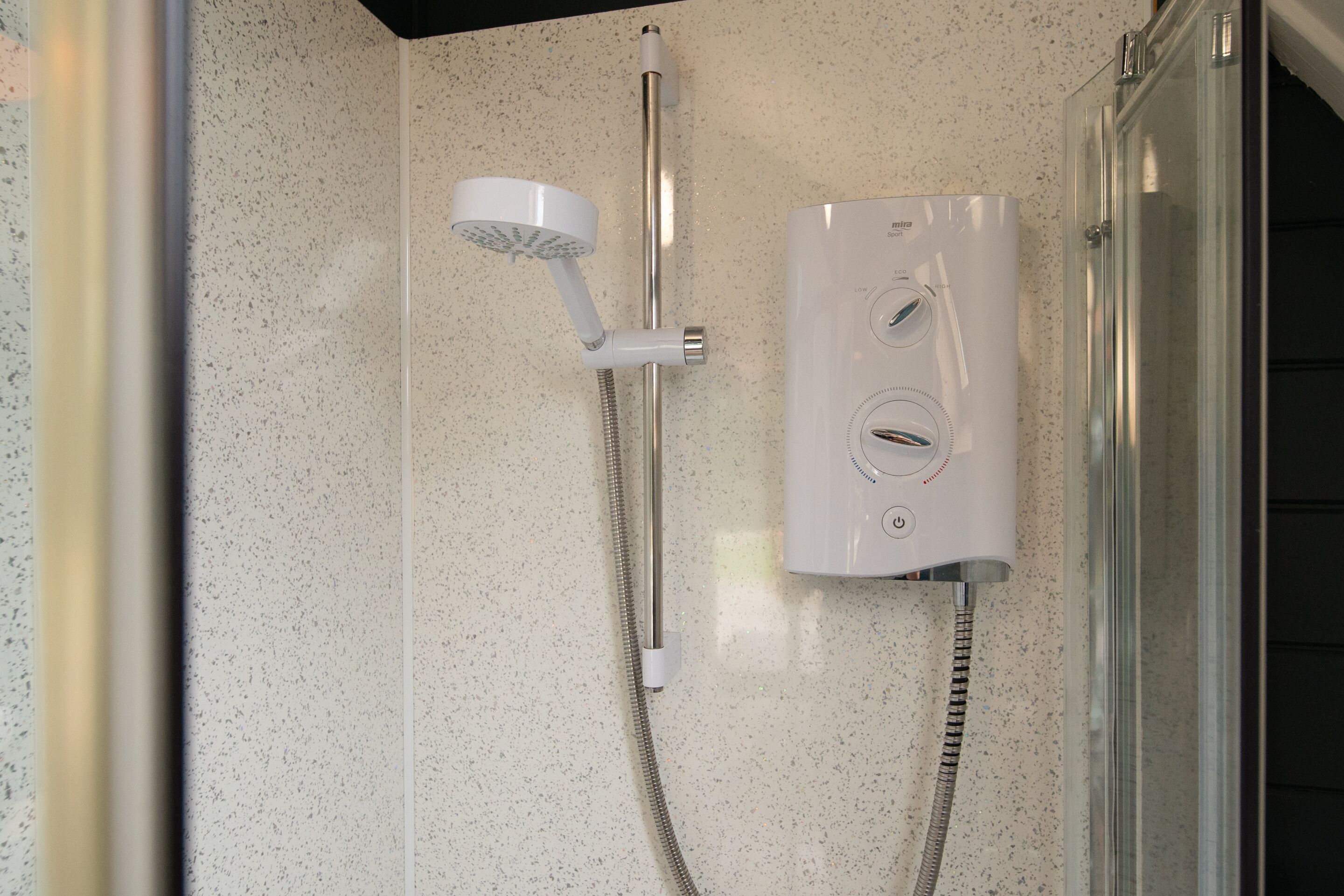 A shower with a handheld showerhead and a wall-mounted control panel.