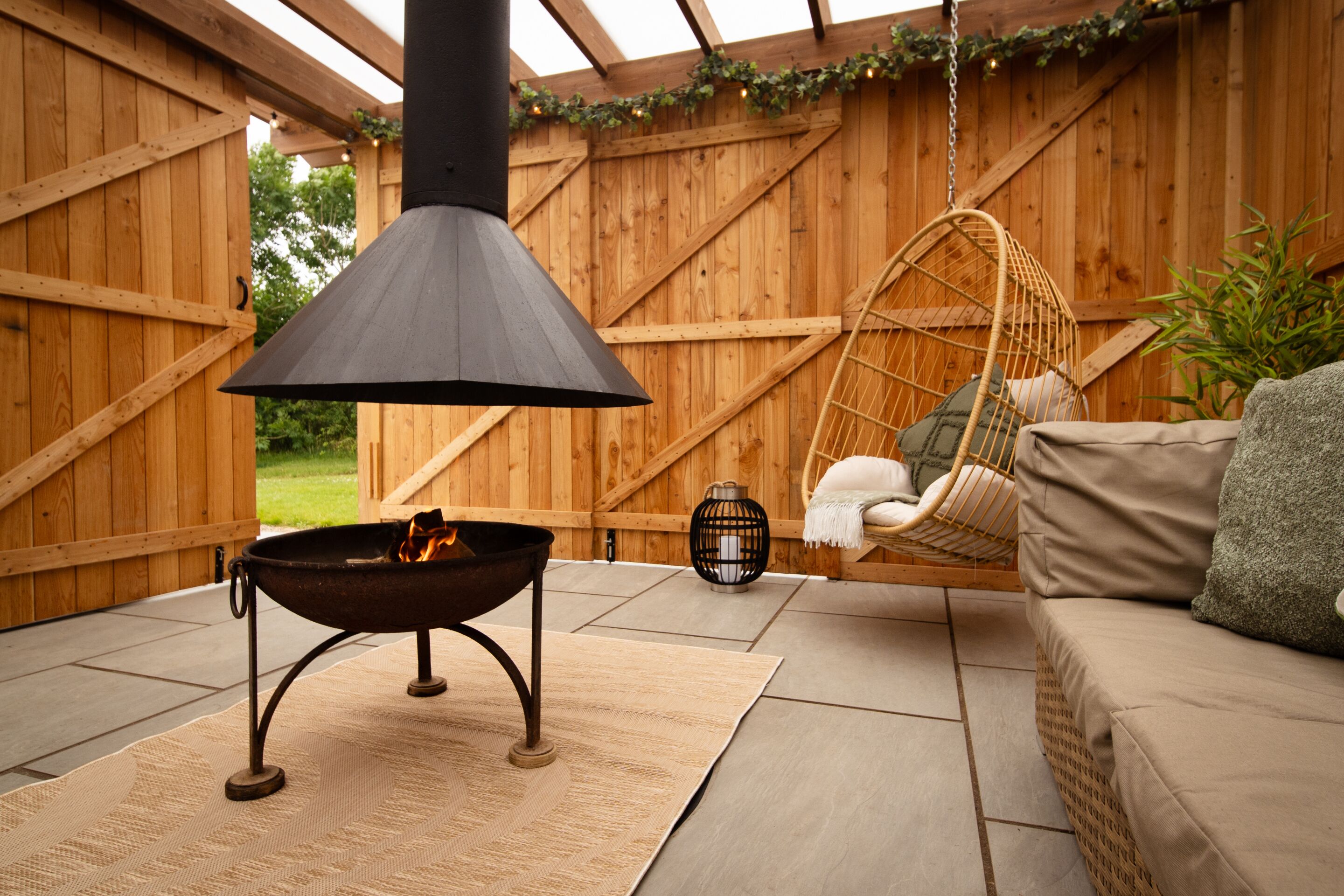 A wooden deck with a fire pit, a hanging chair, and a sofa.