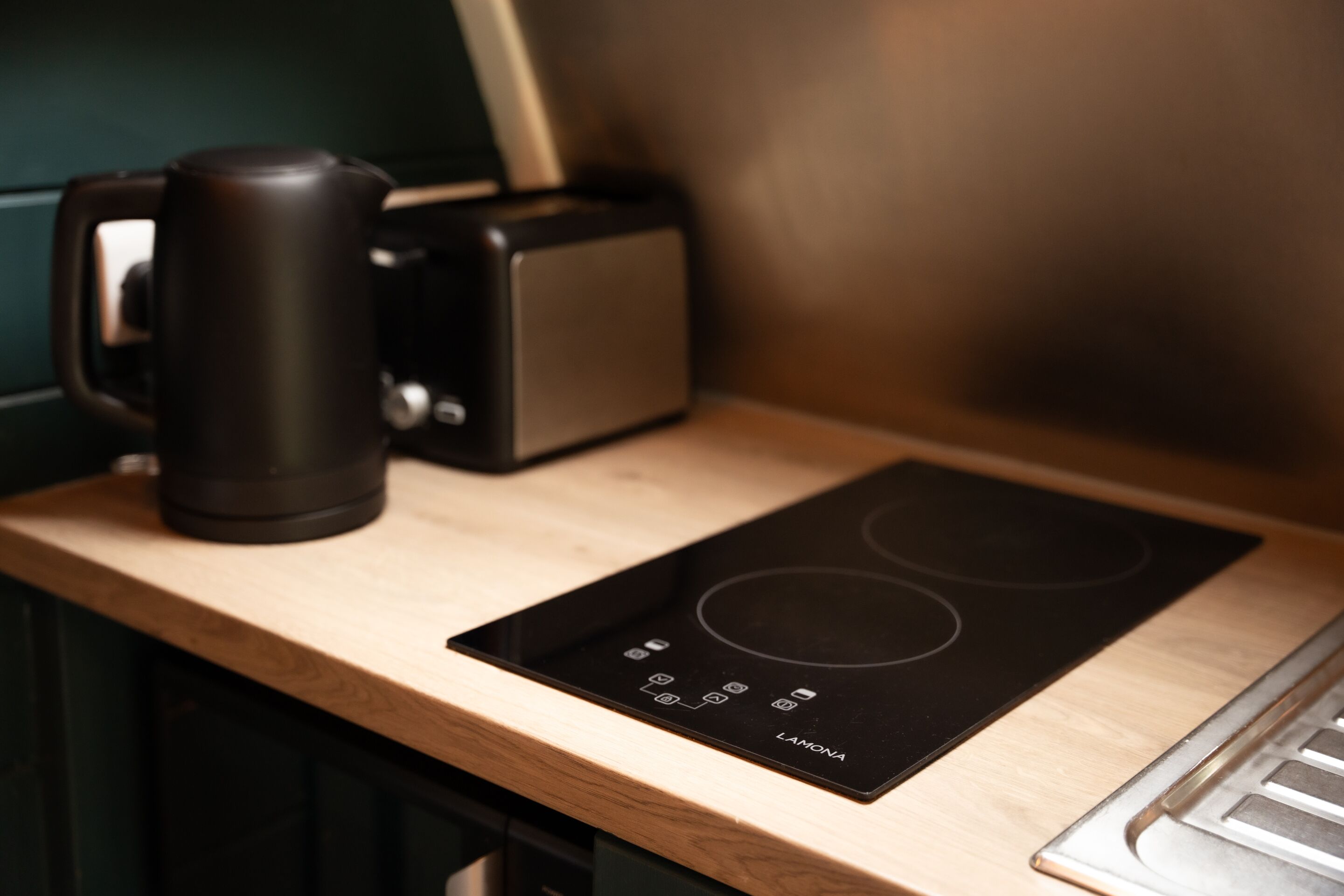 A kitchen with a black induction cooktop, a black coffee maker, and a wooden countertop.