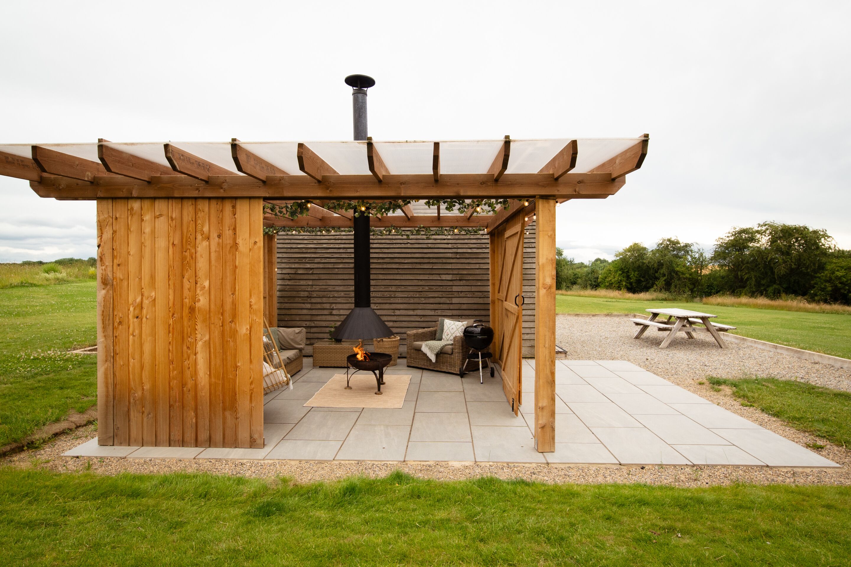 Ein Sitzbereich im Freien mit Holzboden, einer Pergola, einer Feuerstelle und einem Picknicktisch.