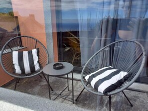 Deux fauteuils en osier avec des coussins à rayures noires et blanches, une petite table ronde et une porte en verre qui reflète une personne.