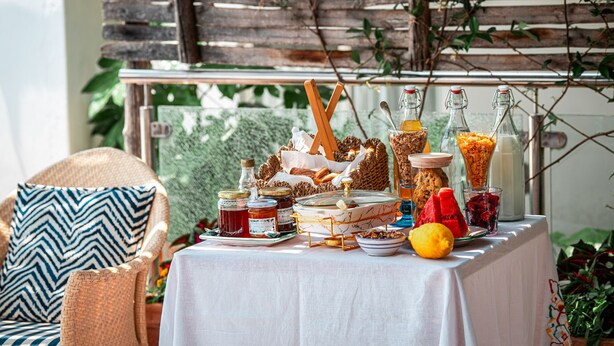 A table set with various food items and drinks, a wicker chair with a patterned cushion, and a wooden fence in the background. - Room-charming Panoramic Suite in the Cen (Positano)