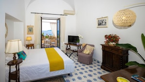 A hotel room with a bed, a television, a chair, a table, and a large window offering a view of the sea. - Room-charming Panoramic Suite in the Cen (Positano)