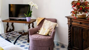 A living room with a flat-screen TV, a purple armchair, a wicker lamp, and a potted plant. - Room-charming Panoramic Suite in the Cen (Positano)